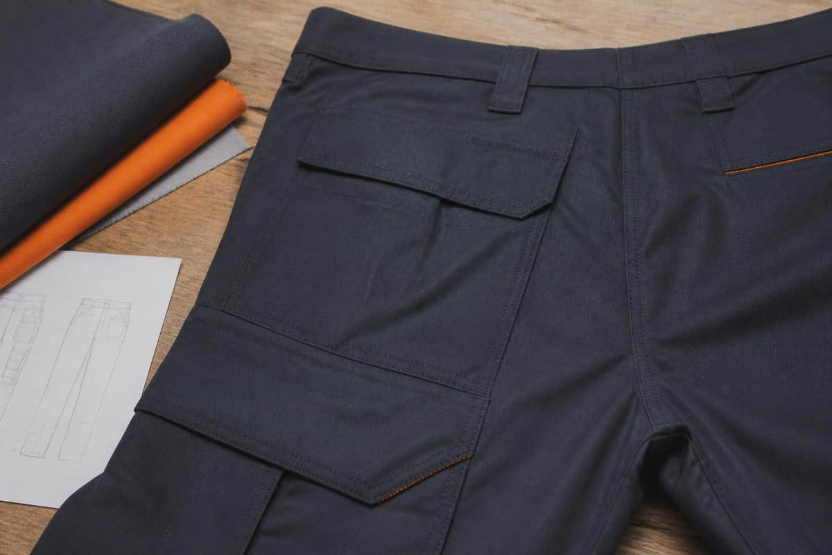 Close-up of a measuring tape wrapped around the waist of a pair of dark work trousers laid flat on a wooden surface